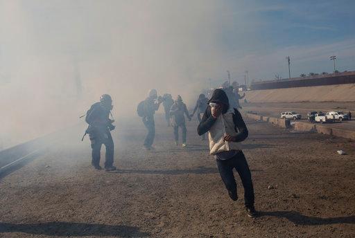 Migrants run from tear gas launched by U.S. agents, amid photojournalists covering the Mexico-U.S. border, after a group of migrants got past Mexican police at the Chaparral crossing in Tijuana, Mexico, Sunday, Nov. 25, 2018. The mayor of Tijuana has declared a humanitarian crisis in his border city and says that he has asked the United Nations for aid to deal with the approximately 5,000 Central American migrants who have arrived in the city. [Photo: AP/Rodrigo Abd]