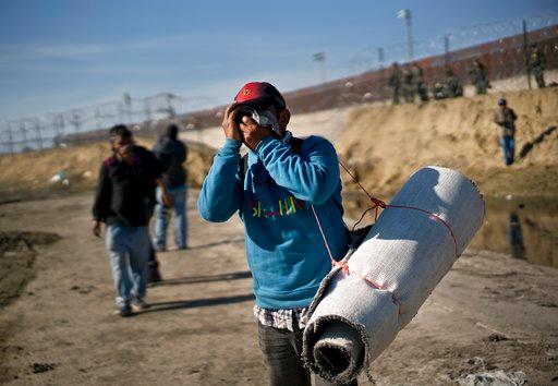 A migrant carrying a roll of carpet wipes his face after U.S. border agents fired tear gas at a group of migrants who had pushed past Mexican police at the Chaparral border crossing in Tijuana, Mexico, Sunday, Nov. 25, 2018. The mayor of Tijuana has declared a humanitarian crisis in his border city and says that he has asked the United Nations for aid to deal with the approximately 5,000 Central American migrants who have arrived in the city. [Photo: AP/Ramon Espinosa]
