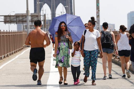 A woman carries an umbrella to shade herself from the heat as a jogger passes by on the Brooklyn Bridge, Wednesday, Aug. 29, 2018, in New York. The National Weather Service says temperatures in the 90s combined with high humidity are pushing the heat index past 100. [Photo: AP/Mark Lennihan]