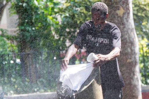 A man uses a park sprinkler to cool off, Wednesday, Aug. 29, 2018, in New York. Dangerously high heat in the Northeastern United States has prompted emergency measures including extra breaks for players wilting at the U.S. Open tennis tournament. [Photo: AP/Mary Altaffer]