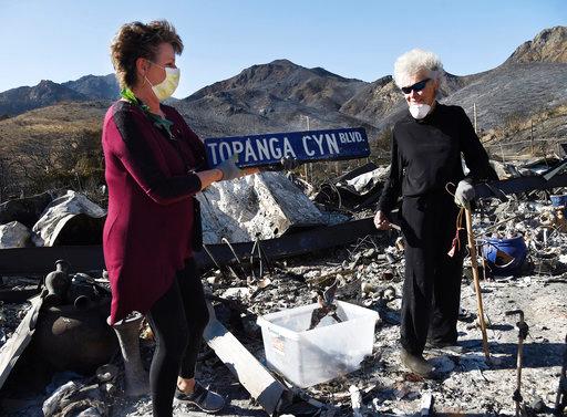 Donna Phillips, left, finds an intact street sign amid the charred possessions of her friend Marsha Maus, right, Sunday, Nov. 11, 2018, after a wildfire tore through the Seminole Springs Mobile Home Park in Agoura Hills, Calif. Maus has been a resident of the neighborhood for 15 years. [Photo: AP]
